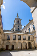 Obraz premium A sunny view of a symmetrical inner patio at El Escorial in Spain, featuring massive granite towers, uniform facades, and a grand basilica entrance. San Lorenzo
