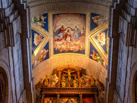 A detailed view of the colorful religious frescoes on the vaulted ceiling above the gilded high altar at El Escorial Basilica in San Lorenzo, Madrid, Spain