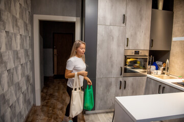 Middle aged woman entering her home kitchen carrying grocery shopping bags. Real everyday life scene showing domestic routine, food shopping, and simple home lifestyle.