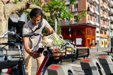 Indian man renting a shared bicycle, returning from grocery shopping with a mesh bag full of vegetables