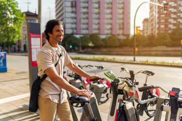 Young asian man standing at a bike sharing station, choosing an electric bicycle for eco friendly urban transport
