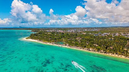 Aerial panoramic view of a luxury tropical resort beach with clear turquoise lagoon water and a speed boat leaving a wake