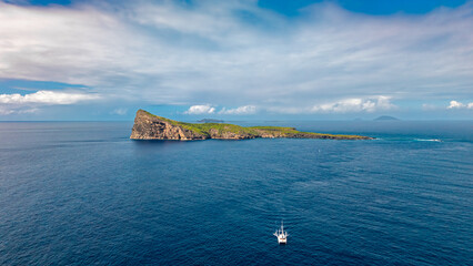 The steep rocky cliffs and green vegetation of Ile aux Fous near Mauritius under a bright, cloudy sky