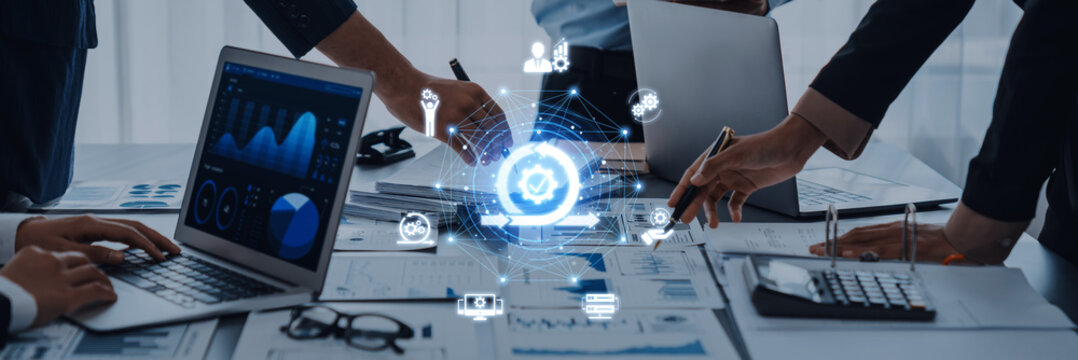 A diverse group of business professionals works together at a desk with laptops and documents, utilizing digital tools for effective data analysis and innovative strategies. Trope - Powered by Adobe