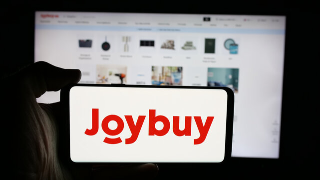 Stuttgart, Germany - 12-17-2025: Person holding cellphone with logo of e-commerce company Joybuy (Joybuy.com) on screen in front of webpage. Focus on phone display.