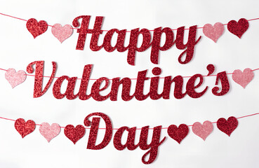 A sparkly red glitter 'happy valentine's day' banner with heart decorations against a white wall