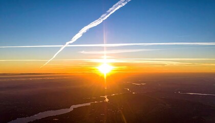 Sunrise over a vast landscape with a river and distant city lights under a clear blue sky with airplane contrails