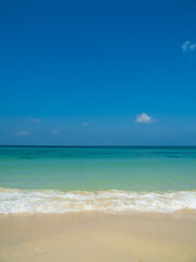 Peaceful vertical tropical sea beach with gentle waves rolling onto golden sand under bright blue sky with fluffy white clouds. relaxing summer scene perfect scene for travel holliday and nature lover