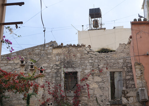 Abandoned stone building in Archanes with pigeons and red climbing plants. Authentic Cretan ruins showcasing textured masonry and the beauty of architectural decay.