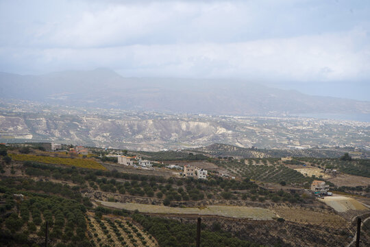 Panoramic view of the Archanes valley from the Phourni (Fourni) archaeological site in Crete. Features ancient olive groves and vineyards stretching toward the sea under a moody sky.