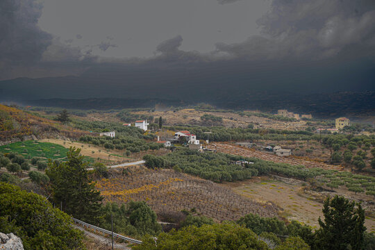 Panoramic view of the Archanes valley from the Phourni (Fourni) archaeological site in Crete. Features ancient olive groves and vineyards stretching toward the sea under a moody sky.