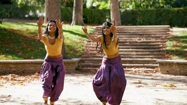 Two young smiling indian women in traditional clothing performing a synchronized energetic bollywood dance routine with graceful hand movements