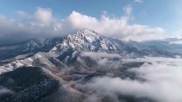 4K Aerial view of majestic snowcapped mountain peak emerging from thick lowlying clouds and fog during winter in a vast mountain range landscape under a blue sky video