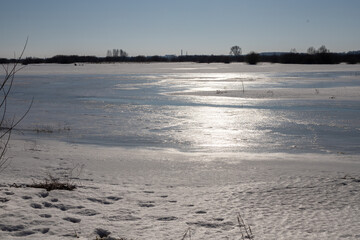 Frozen river covered in ice. Tranquil winter landscape in the rays of the evening sun.