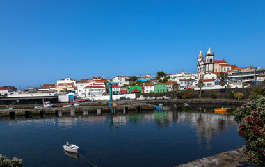 Scenic view of S&atilde;o Mateus da Calheta harbor on Terceira Island, Azores, Portugal, featuring colorful houses, fishing boats, calm waters, and a historic church under a clear blue sky
