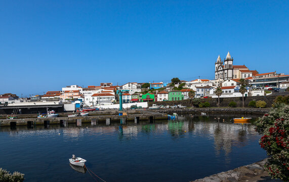 Scenic view of S&atilde;o Mateus da Calheta harbor on Terceira Island, Azores, Portugal, featuring colorful houses, fishing boats, calm waters, and a historic church under a clear blue sky