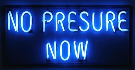Bright blue neon sign displays text. Words no pressure now illuminate dark background. Simple, direct message conveyed.