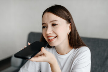 young beautiful caucasian brunette woman recording voice message, smiling widely, casual clothes, white T-shirt, talking by smartphone