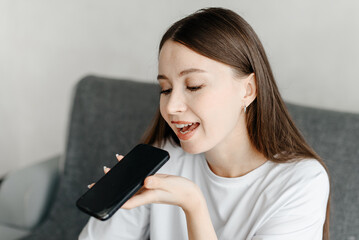 young beautiful caucasian brunette woman recording voice message, smiling widely, casual clothes, white T-shirt, talking by smartphone