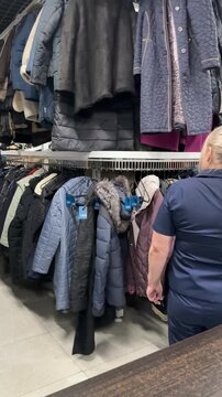 Rows Of Winter Coats Hanging, Shop Owner Sorting Preloved Inventory Beneath Crowded Rack, Mixed Textures Wool Denim Leather, Muted And Bright Colors, Cozy Cluttered Atmosphere, Sustainable.