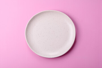 An empty round ceramic plate on a pink background as a kitchen utensil. An empty plate