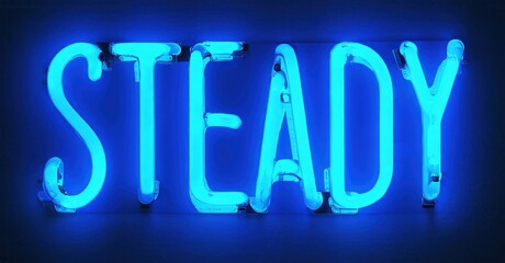 Bright blue neon sign spells STEADY. Dark background emphasizes glowing letters. Simple, bold typography creates strong visual impact.