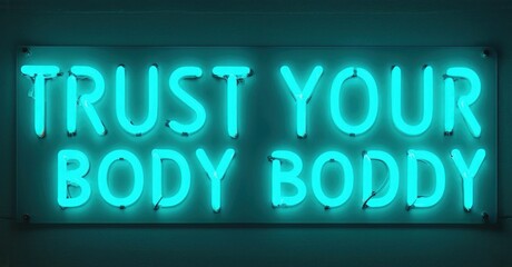 Fototapeta premium Bright neon sign displays text. Turquoise glow illuminates dark background. Message promotes self acceptance, body positivity.