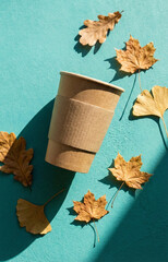 Eco coffee cup and autumn leaf against a teal background. Autumn paper coffee cup and fall leaves on vibrant teal background.