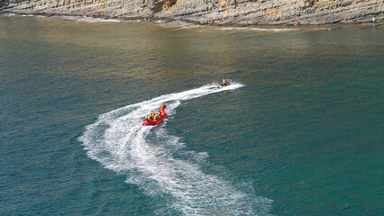 A popular water attraction on the seashore. A group of people rides on a water tube towed by a jet ski. © ROMAN DZIUBALO