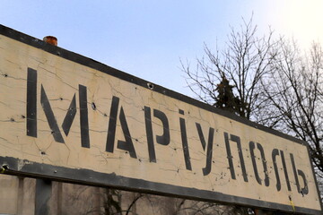 Obraz premium War in Ukraine. A road sign with inscription in Ukrainian - Mariupol, pierced by bullets during war in Ukraine.