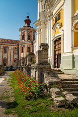 Fototapeta premium Baroque architectural details on the facade of the former Jesuit Collegium building in Kremenets, Ukraine, featuring a colorful flowerbed along its aged stone steps and walls