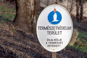 Nature protection area sign located in Hungary near a forest with trees and a clear sky