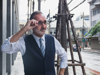 business man senior in formal suit stand confidently with ooking ahead on city street. Modern building, palm trees, and urban element in background create professional and metropolitan atmosphere.