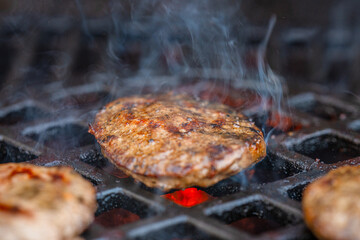 burger patty smoking over glowing coals on barbecue grill.