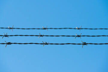 Barbed wire fence lines against clear blue sky.