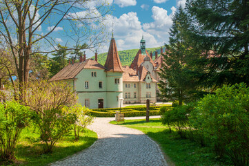 Picturesque Beregvar (Shenborn's) Palace surrounded by lush greenery and trees in springtime. Cobblestone path leads to the elegant white building with red-tiled roofs and turrets © haidamac