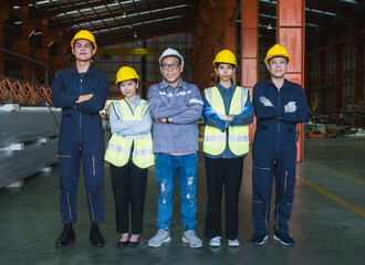 group five industrial worker standing together in factory setting, wearing safety helmets and...