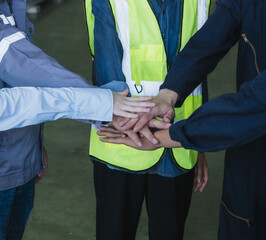 group five industrial worker wearing safety helmet and reflective vest standing circle inside factory placing their hands together center symbolize teamwork collaboration in safe working environment.