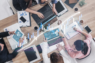 A diverse business team collaborates on data analysis and strategy planning, surrounded by laptops, documents, and coffee cups, showcasing graphs and charts. Impute