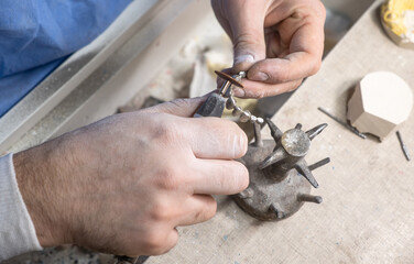 Dental technician processing metal-ceramic crowns on dental model using rotary tool in laboratory, part of prosthodontic crown creation and adjustment.