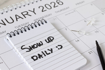 Show up daily, handwritten quote in a notebook on 2026 calendar. Close-up. The concept of growth, motivation, progress, and success.