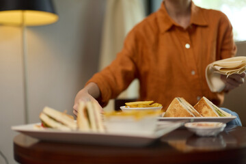 Woman serving healthy sandwiches on a wooden table, showcasing fresh ingredients and a cozy...