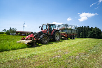 Obraz premium Grünfutterernte im Allgäu, Traktor mit vorgebautem Mähwerk und Ladewagen bei der Grasernte.