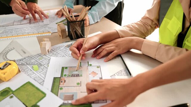 Smart architect and safety engineer discussion about building blueprint on table with architectural document, measurement tools and wooden block scatter around at modern office. Closeup. Delineation.