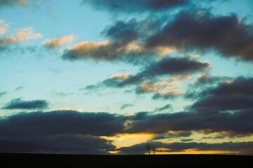 Landschaftspanorama mit zwei B&auml;umen auf Ackerfeld vor dramatischem Wolkengebilde an Himmel mit goldgelbem Licht bei Sonnenuntergang am Abend im Winter