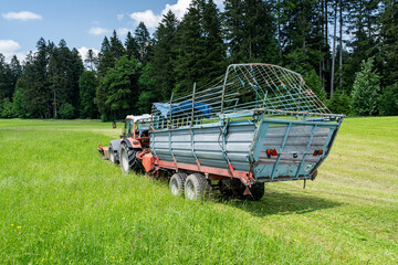 Gr&uuml;nfutterernte im Allg&auml;u, M&auml;hren und ernten von frischem Gras mit Vorbaum&auml;hwerk und Ladewagen.