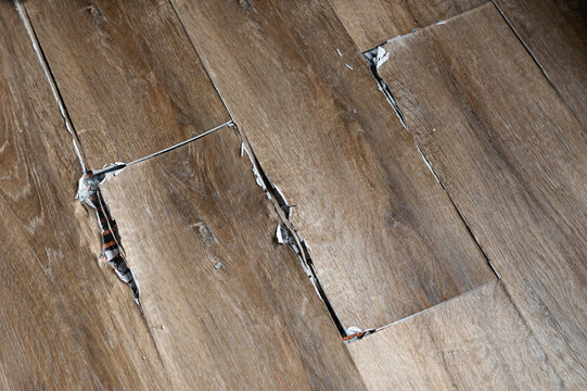 buckled laminate floor with torn planks and visible crack caused by heated floor expansion. closeup of damaged floor covering with lifted edges