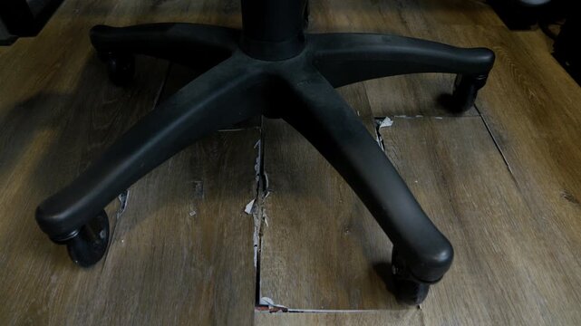 buckled laminate floor with torn planks and visible crack caused by heated floor expansion. closeup of damaged floor covering with lifted edges on which stands an office chair on wheels