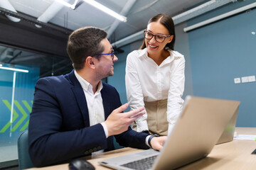 Positive business people man and woman software developers working as team in office, discussing work plans using laptop