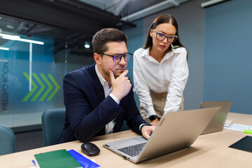 Creative serious business colleagues meeting in office using laptop and talking about new plans, checking reports